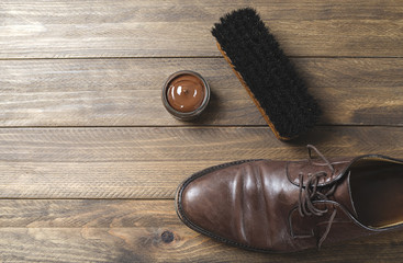 Dirty brown shoe next to brush and cream on wooden table. Horizontal shoot.