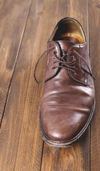 Used and dirty brown shoe on brown wooden table. Vertical shoot.