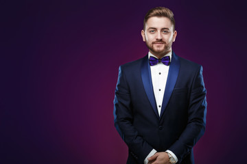 Handsome man in tuxedo and bow tie looking at camera. Fashionable, festive clothing. emcee on dark background