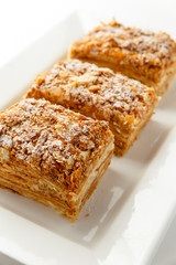 French Napoleon Cake of puff pastry with sour cream on a white plate close-up. Nutritious dessert. Selected Focus