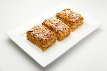 French Napoleon Cake of puff pastry with sour cream on a white plate close-up. Nutritious dessert. Selected Focus