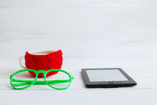 E-book, glasses and a red cup of tea on a white background. 