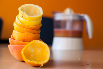 Pile of freshly squeezed citruses and a squeezed orange in front and the juicer full of juice in the background