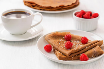 Whole wheat chocolate crepes with fresh raspberries on white pla