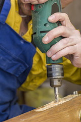 Carpenter makes a hole in old wooden door the mortise lock for by using power drill. Close-up.
