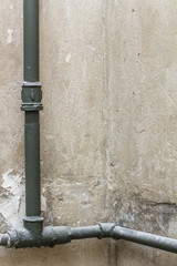 On the wall in a corner an old heating pipes are covered with dust, without a radiator.