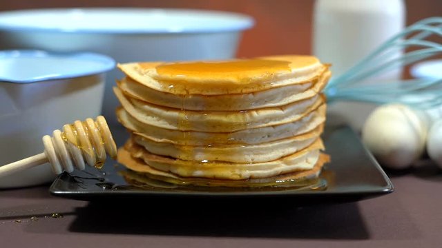 Shrove Pancake Tuesday, last day before Lent, stack of pancakes closeup in front of blue enamel bowls, eggs, whisk and cooking utensils, short dolly reveal to static.
