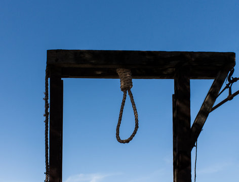 Wooden hangman's gallows with rope noose against blue sky