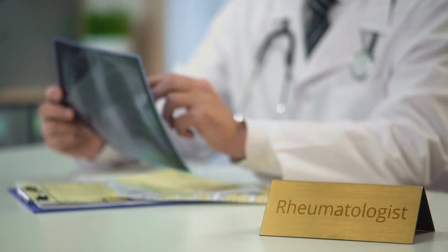 Experienced rheumatologist looking at x-ray image and writing down diagnosis