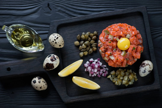 Black wooden serving board with salmon tartar, high angle view