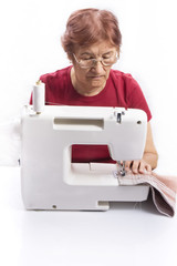 elderly woman sews on the sewing machine 