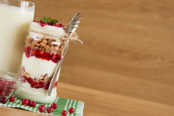 Healthy breakfast - layered dessert with yogurt, granola, jam, raspberries, cranberries and mint on wooden background