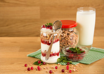 Healthy breakfast - layered dessert with yogurt, granola, jam, raspberries, cranberries and mint on wooden background