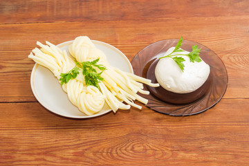 Two varieties of mozzarella cheese with parsley on wooden surface