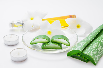 Fresh aloe vera slices with leaf, flowers, candels and oil on wh