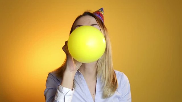 Beautiful girl blowing balloons on a yellow background
