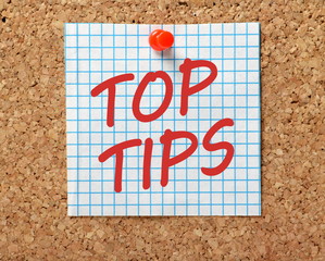 The words Top Tips in red text on a piece of square graph paper pinned to a cork notice board as a...