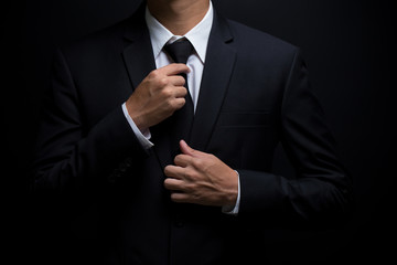Man in black suit and adjusting his necktie - obrazy, fototapety, plakaty