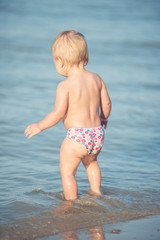 Baby playing on the sandy beach and in sea water. Cute little kid with toys on sand tropical beach. Ocean coast.