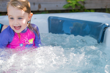Cute girl caucasian toddler blonde hair blue eyes bright rash vest playing in water full of joy and happiness learning to swim and splashing about in the sun in the jacuzzi 