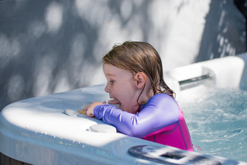 Cute girl caucasian toddler blonde hair blue eyes bright rash vest playing in water full of joy and happiness learning to swim and splashing about in the sun in the jacuzzi playing with shells 