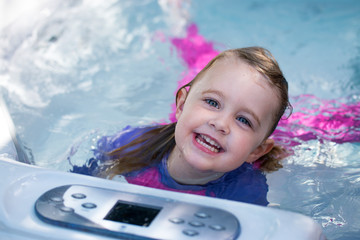 Cute girl caucasian toddler blonde hair blue eyes bright rash vest playing in water full of joy and happiness learning to swim and splashing about in the sun in the jacuzzi  - obrazy, fototapety, plakaty