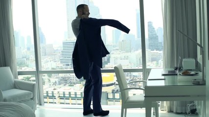 Businessman putting on jacket standing by window at home
