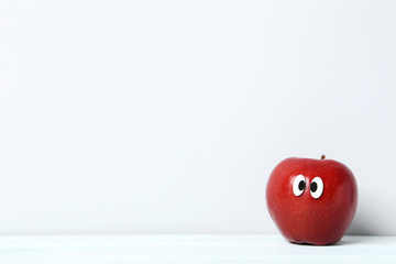 Red apple with googly eyes on grey background