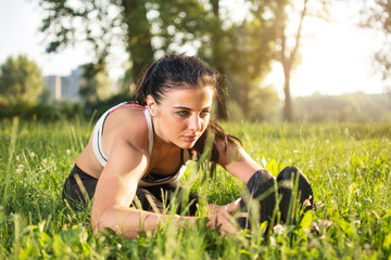 Young woman stretching before exercise in park at sunset.