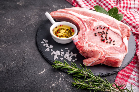 Raw meat on dark background. Raw pork steak with herbs, oil and spices. Cooking meat