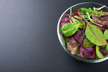 Fresh green salad with spinach, arugula, chard leaves, lettuce. Mixed salad leaves on dark background. Healthy food, healthy lifestyle and diet concept. Top view
