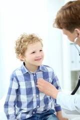 Pediatrician examining school boy. Doctor using stethoscope to listen to kid chest checking heart beat.