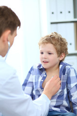 Obraz premium Young male doctor auscultating a little boy by stethoscope.