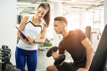 Tuinposter Female personal trainer showing exercise results to her male client in a gym. © Bojan