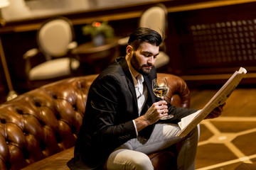 Handsome man drinking white wine and reading newspaper