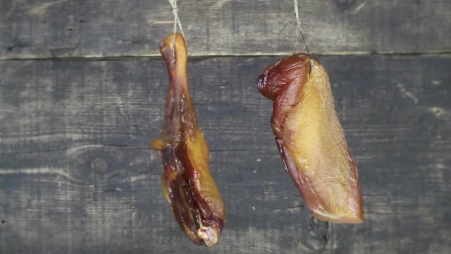 Smoked Chicken Meat Hanging On a Rope And Swaying Against Wooden Background