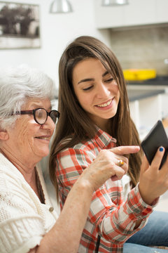 Grandmother Showing Something On Mobile Phone To Her Young Granddaughter.