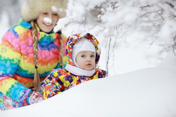 little girl and mother sit and play in the snow in the park