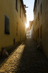 Empty narrow cobblestone street lit by morning sun. Old street in ancient town of Rothenburg ob der Tauber in Germany, Europe.
