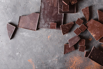 Chocolate  chunks and cocoa powder. Chocolate bar pieces.  A large bar of chocolate on gray abstract background. Background with chocolate. Slices of chocolate, Sweet food photo concept. Copyspace