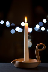 Portacandela con candela bianca accesa su superficie nera e sullo sfondo luci notturne