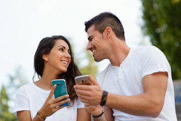 Young couple dating and using their smartphones. Man and woman comparing cellphones outdoor. Modern...