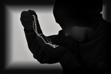 Female robber with black tights over her head holding and looking at the stolen jewellery. Black and white. Low key. Selective focus.   - obrazy, fototapety, plakaty