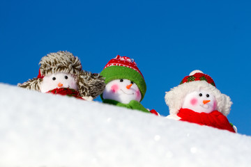 The winter, Christmas - three happy snowmen stand against the background of the blue sky.