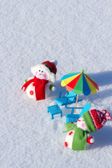 Two cute snowman sunbathing in the snow. Paper beach chairs and a  umbrella. Winter background