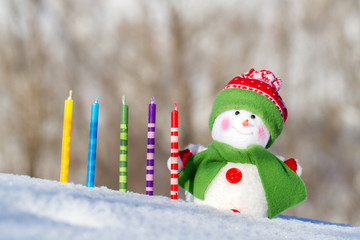 Fototapeta premium Bright snowman and festive candles on a winter background. Blue sky. White snow.