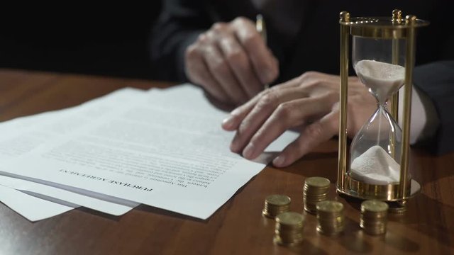 Male buyer or seller signing purchase agreement, money and hourglass on table