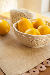 White bowl with lemons on tablecloth and wooden table