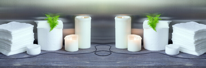 White paper towel, toilet paper, paper tissues, cotton disks on wooden table with burning candles. Kitchen disposables, toiletries. Toned image. Wide panoramic image.