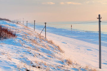 Perspective view of snowy poles in the sunset time. Coast of Baltic Sea.